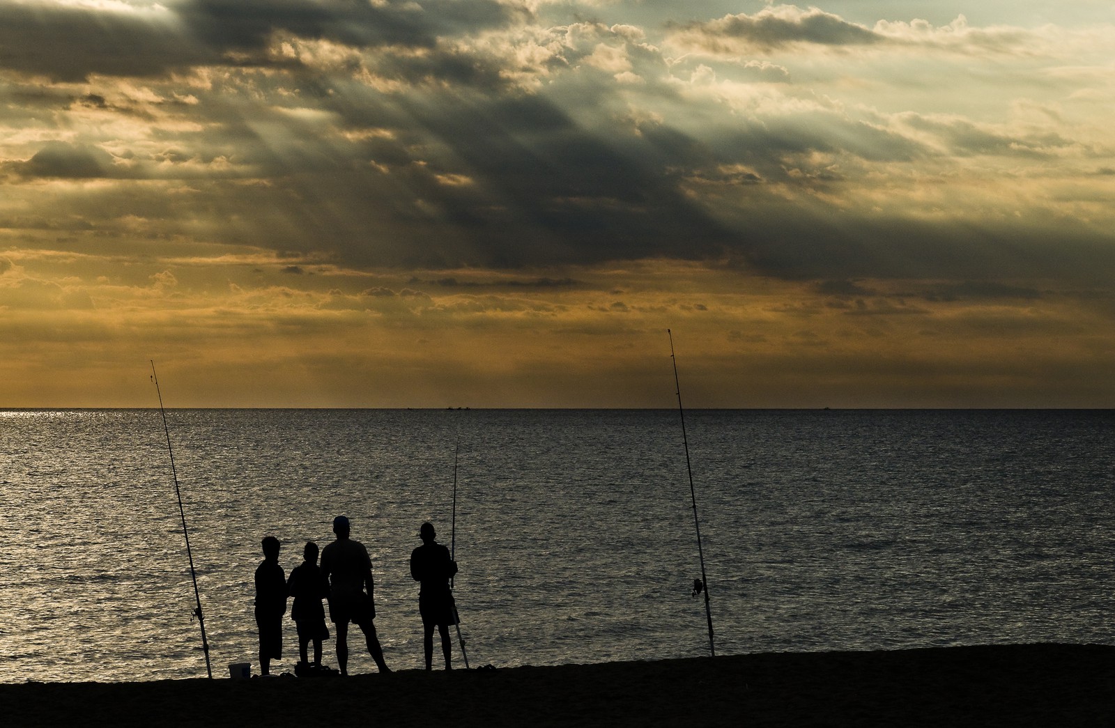 Silhouettes de pêcheurs à la ligne sur la plage au lever du soleil. - Silhouettes of anglers on the beach at sunrise. Silhouettes de pêcheurs à la ligne sur la plage au lever du soleil. - Silhouettes of anglers on the beach at sunrise.